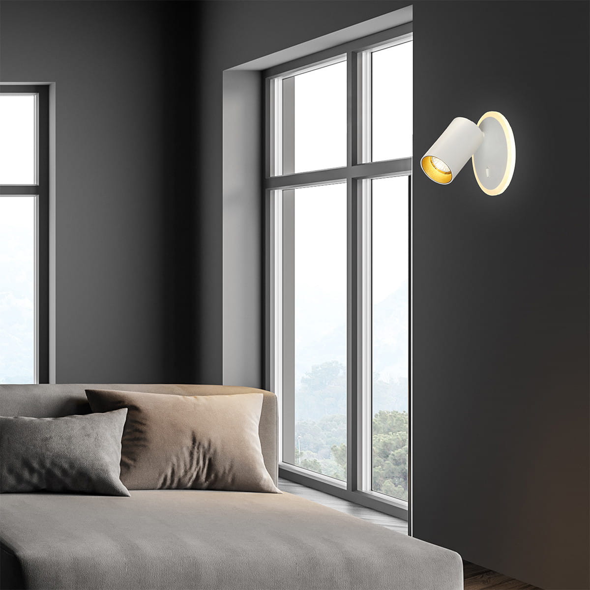Kinkiet Parma 1xGU10 + 1xLED w kolorze białym, zamontowany na szarej ścianie, skierowany w dół. Obok widoczna szara sofa z poduszkami. Jasne okna w tle, tworzące przytulną atmosferę.