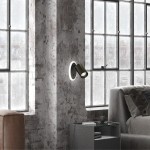 Kinkiet Parma w kolorze czarnym z jedną oprawą GU10 i diodą LED, zamontowany na ścianie. Produkt ma cylindryczny kształt z okrągłym, białym otoczeniem, umieszczony obok szarej sofy i stolika w industrialnym wnętrzu.