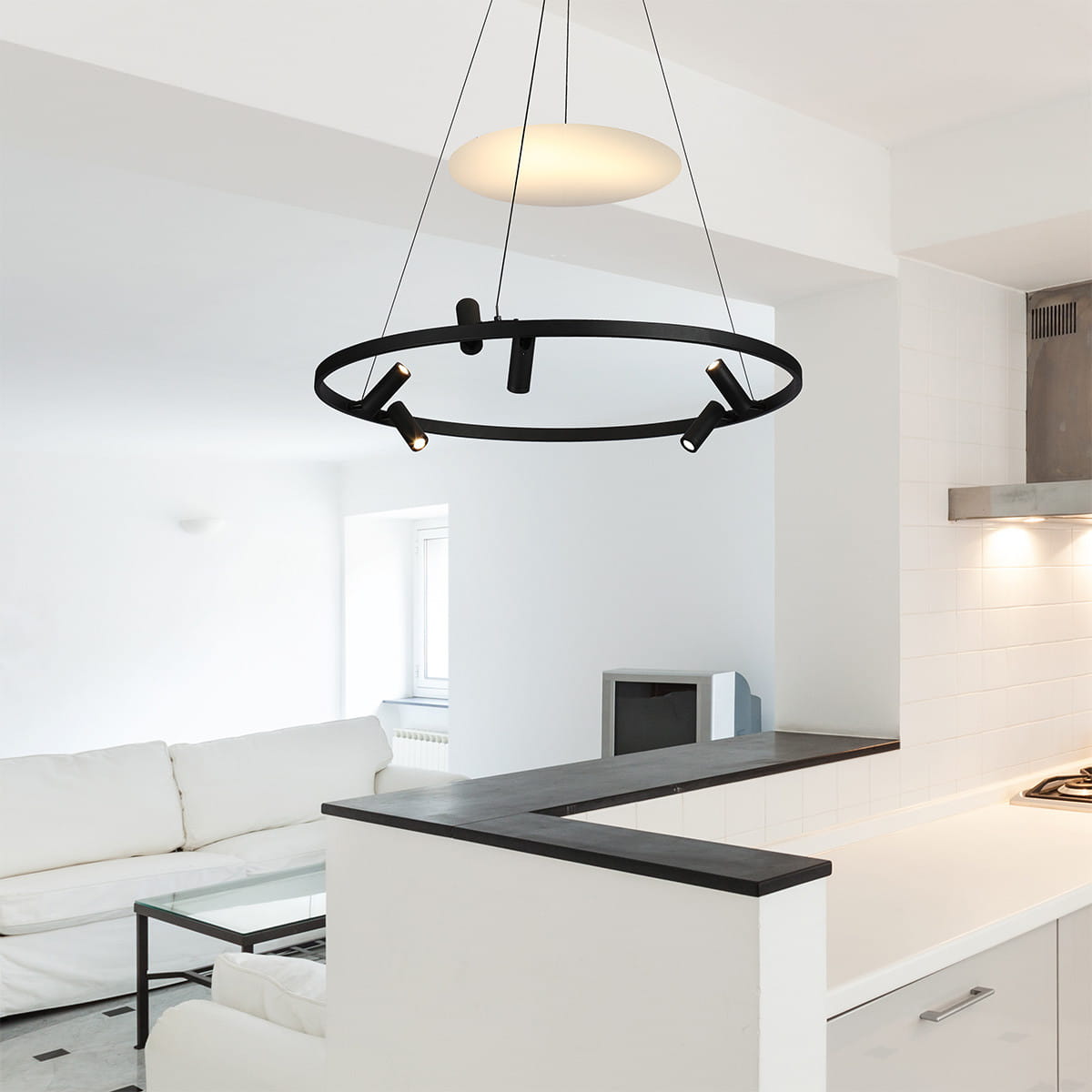 Lampa wisząca Almeria w kolorze czarnym z sześcioma źródłami LED (18W) w minimalistycznym okrągłym kształcie, zawieszona na cienkich linkach. Oświetlenie umieszczone w różnych kierunkach, w nowoczesnym wnętrzu z jasnymi ścianami i meblami.