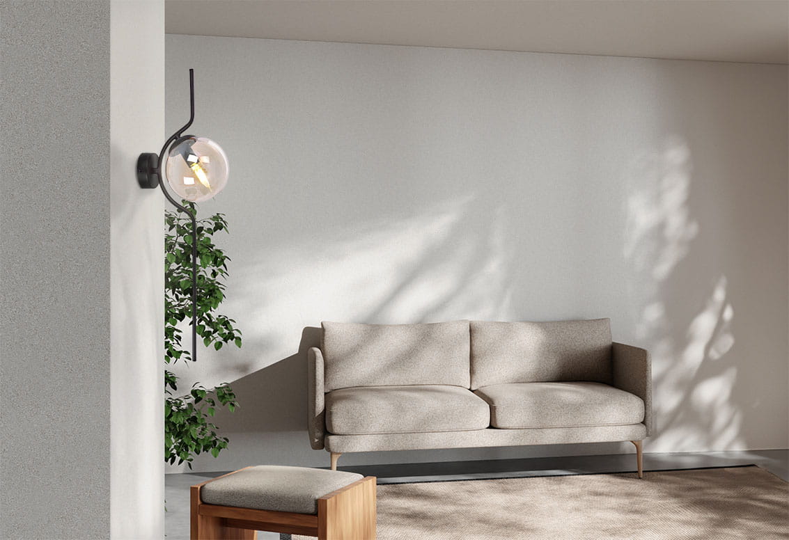 Kinkiet Vela 1xE14 w kolorze czarnym z bursztynowym kloszem, zamontowany na ścianie obok jasnej kanapy. Lampa ma zaokrąglony kształt klosza i stylowy, minimalistyczny design, otoczona roślinnością, co podkreśla nowoczesne wnętrze.