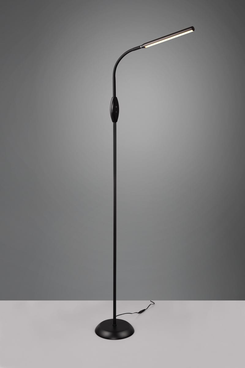 Czarna lampa podłogowa Toro z jedną diodą LED o mocy 5W. Ma smukły, zakrzywiony kształt, z okrągłą podstawą i włącznikiem w centralnej części. Ujęcie frontalne, na jednolitym tle. Idealna do użytku w różnych aranżacjach wnętrz.