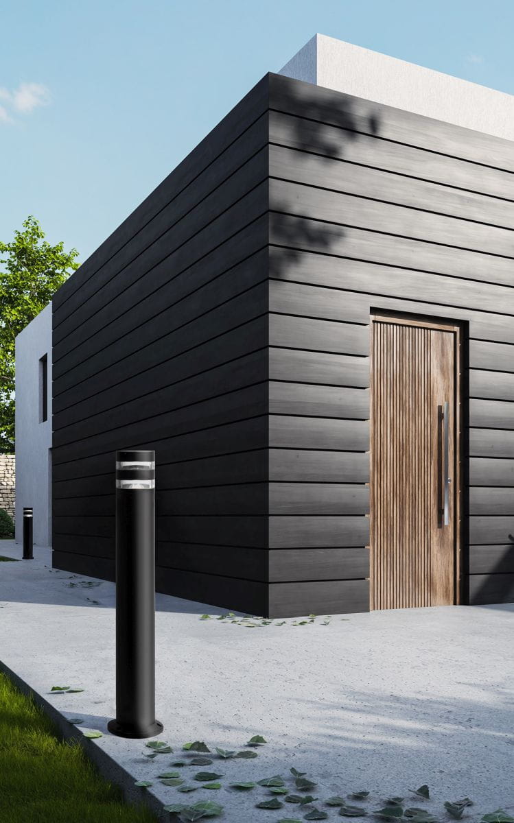 Czarna lampa ogrodowa Solin, stojąca, z oprawą na żarówkę E27, z widoczną szklaną częścią u góry. Ustawiona na betonowej nawierzchni, obok drewnianych drzwi w nowoczesnym budynku, otoczona zielenią i drobnymi liśćmi.