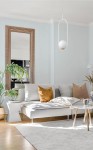 Lampa wisząca Malta 1xE14 w białym kolorze, o minimalistycznym kształcie, zawieszona na cienkim przewodzie. W tle salon z szaro-beżową sofą, poduszkami w odcieniach brązu, białym stolikiem i rośliną. Jasne, neutralne tło.