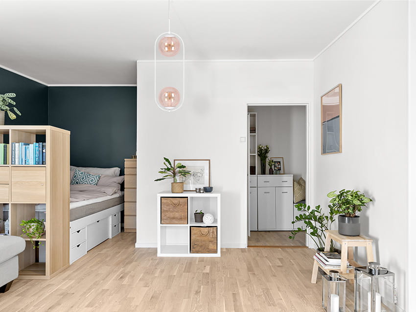 Lampa wisząca Alma z dwoma kloszami E14 w kolorze białym i bursztynowym, zawieszona na białym suficie. W tle jasne wnętrze z drewnianą podłogą, meblami oraz roślinnością, co tworzy przytulną aranżację.