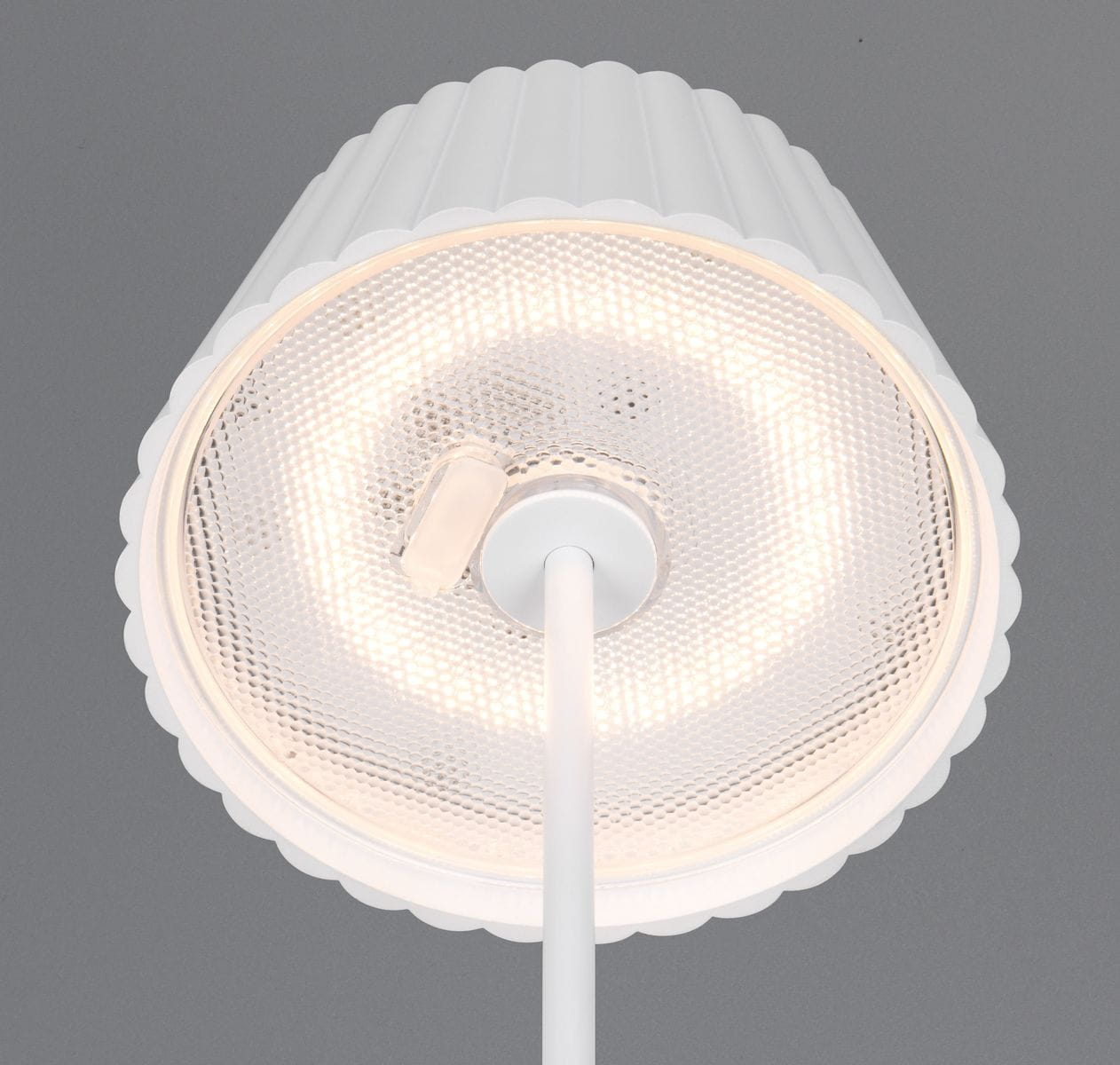 Lampa stołowa Suarez zewnętrzna, biała, z kloszem w kształcie falbany. Widoczny okrągły panel LED o mocy 1,5W, zamontowany na cienkiej podstawie. Ujęcie z góry, na szarym tle.