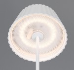 Lampa stołowa Suarez zewnętrzna, biała, z kloszem w kształcie falbany. Widoczny okrągły panel LED o mocy 1,5W, zamontowany na cienkiej podstawie. Ujęcie z góry, na szarym tle.