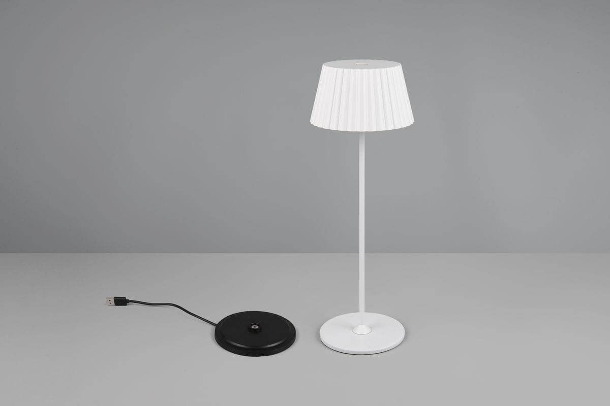 Lampa stołowa Suarez zewnętrzna 1xLED/1,5W w kolorze białym. Posiada biały klosz o fałdowanej fakturze na smukłej, białej nodze oraz czarną podstawę z kablem USB. Produkt ustawiony w pozycji pionowej, na jednolitym tle.