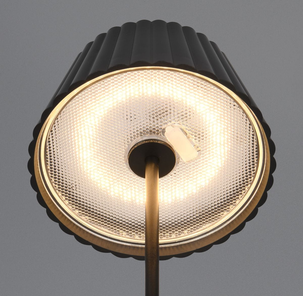 Czarna lampa stołowa Suarez z zewnętrznym kloszem, z LED o mocy 1,5W. Klosz ma teksturowaną powierzchnię z wypukłymi detalami i złotym wykończeniem wewnątrz. Ujęcie z góry, pokazujące źródło światła oraz konstrukcję lampy.
