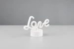 Lampa stołowa Amor w białym kolorze, z napisem Love wykonanym w formie dekoracyjnej. Ustawiona na okrągłej podstawie, z widocznym źródłem światła LED o mocy 1W. Tło w odcieniu szaro-beżowym.