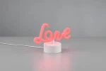 Lampa stołowa Amor w kształcie napisu Love, wykonana z różowego, elastycznego materiału, osadzona na białej, okrągłej podstawie. Widoczny przewód zasilający. Produkt ustawiony na jednolitym tle.