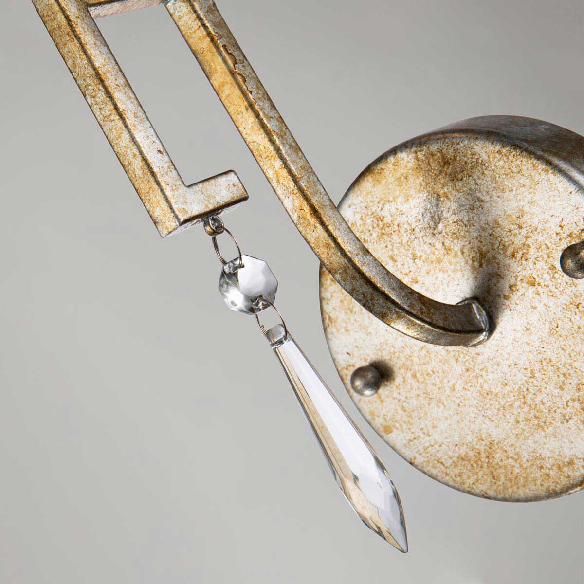 Lemuria kinkiet w kolorze starego złota z metalową podstawą. Uchwyt o prostym kształcie z ozdobnym kryształowym wiszącym detalem. Kinkiet montowany na ścianie, widoczny z bliska.