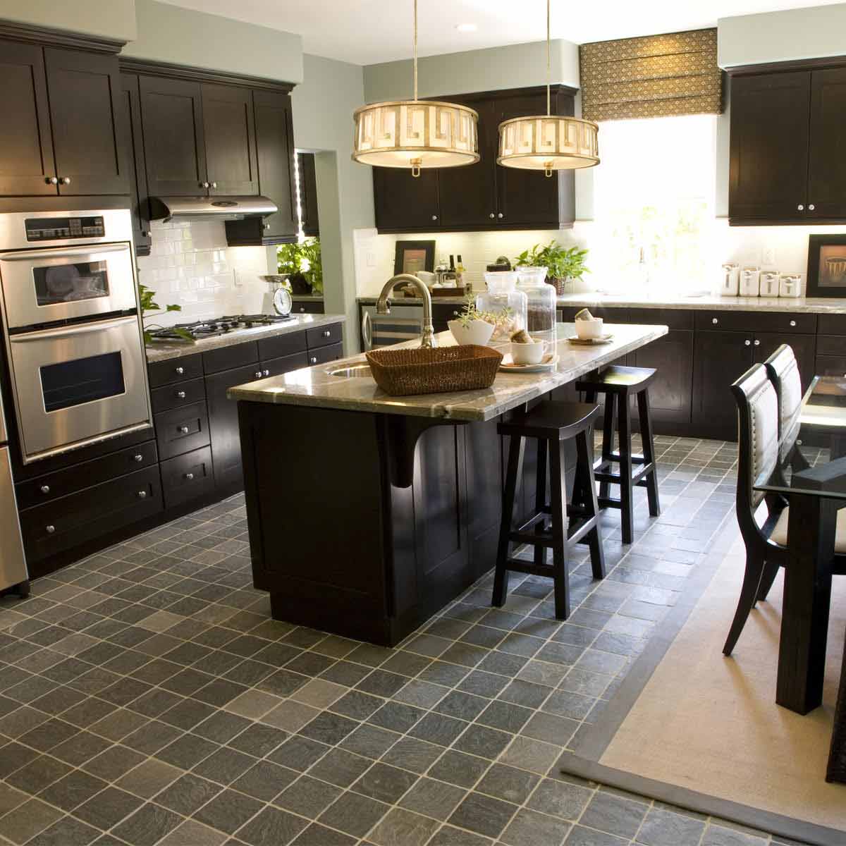 Lemuria lampa wisząca z trzema źródłami światła E27 w kolorze starego złota. Produkt zawieszony nad wyspą kuchenną, w otoczeniu ciemnych mebli i marmurowego blatu. Wnętrze jasne z roślinami i dodatkami dekoracyjnymi.