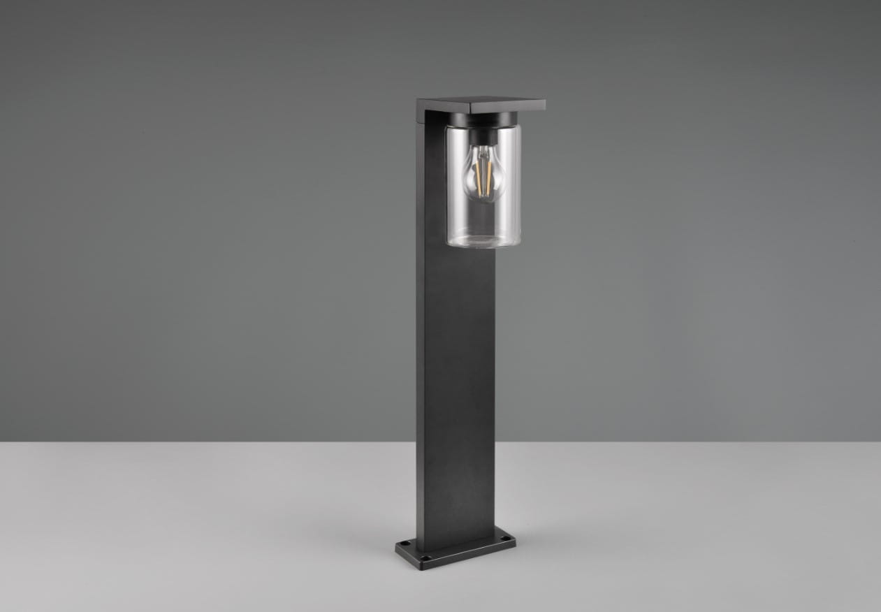 Czarna lampa stojąca Ardila H65 LED z przezroczystym kloszem, wyposażona w czujnik zmierzchu. Produkt ma prostokątną podstawę i minimalistyczny design, umieszczony na jasnym tle. Klosz eksponuje żarówkę, nadając nowoczesny wygląd.