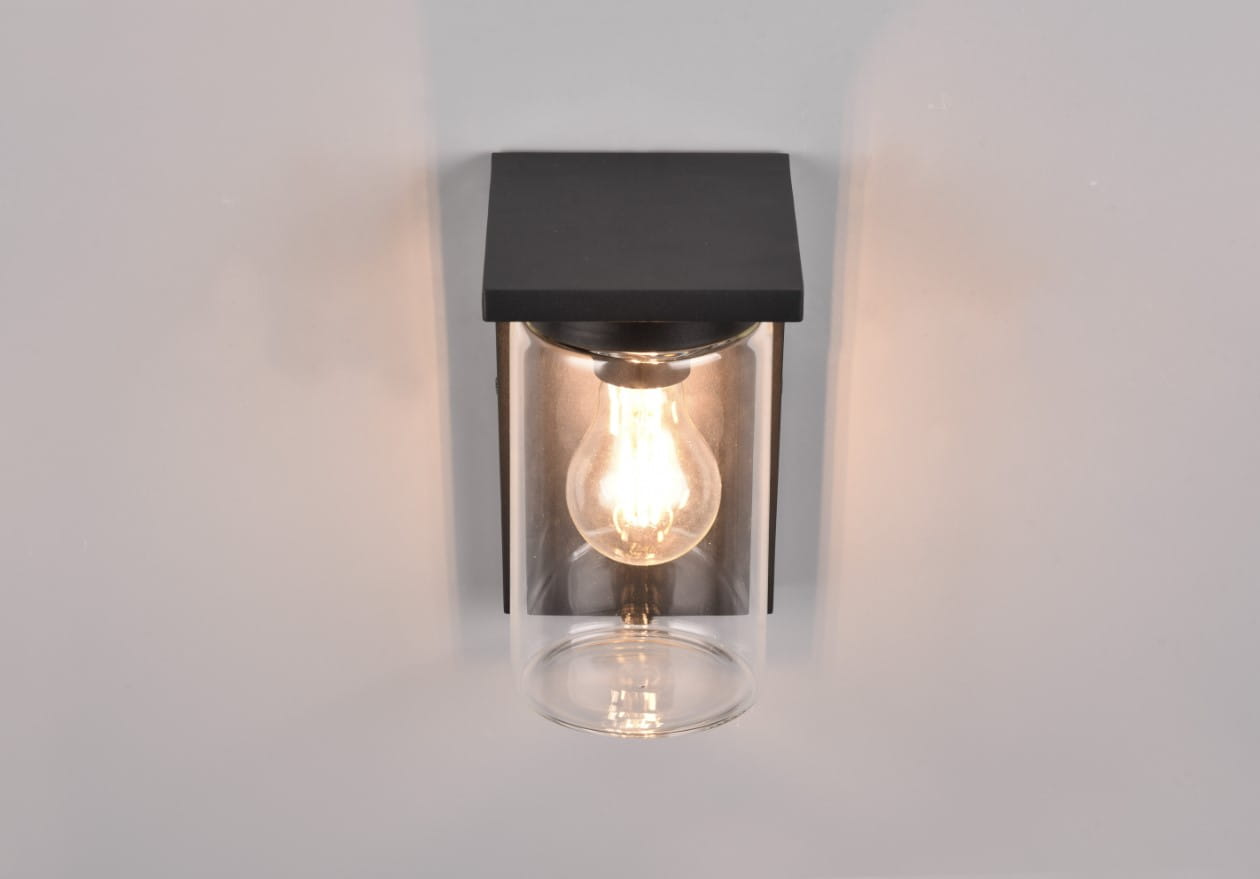 Kinkiet zewnętrzny Ardila w kolorze czarnym, z czujnikiem zmierzchu. Posiada prostokątną, matową podstawę oraz szklany klosz, w którym widoczna jest żarówka. Montowany na ścianie, w frontalnym ujęciu.