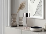Lampa stołowa Jeff z chromowanym wykończeniem, 1xLED/1,5W, stojąca na okrągłej podstawie. W tle widać szklane wazony oraz ceramiczny talerz, na stonowanym tle z grafiką.