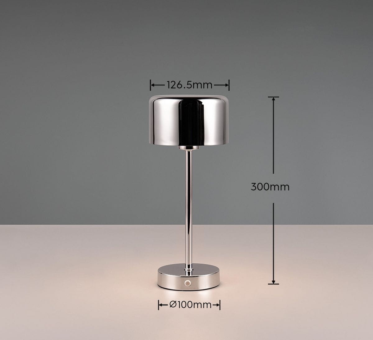 Lampa stołowa Jeff w kolorze chromu, wysokość 300 mm, średnica podstawy 100 mm. Okrągła głowica o wysokości 126,5 mm, umieszczona na cienkiej, prostej nodze. Prosta konstrukcja na jednolitym tle.