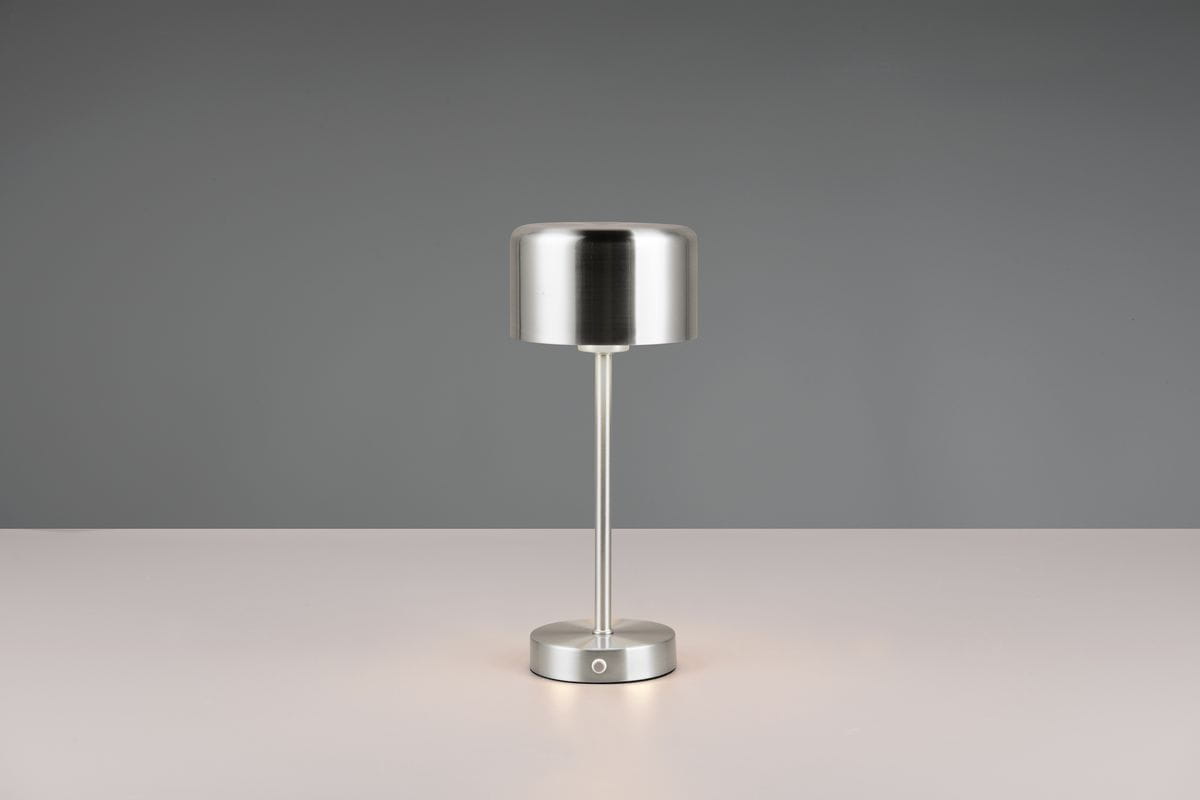 Lampa stołowa Jeff w kolorze niklowym, z okrągłą podstawą i cylindrycznym kloszem. Ujęcie frontalne, produkt stoi na jednolitym tle. Widoczny przycisk w podstawie, lampa z jednym źródłem LED o mocy 1,5W.
