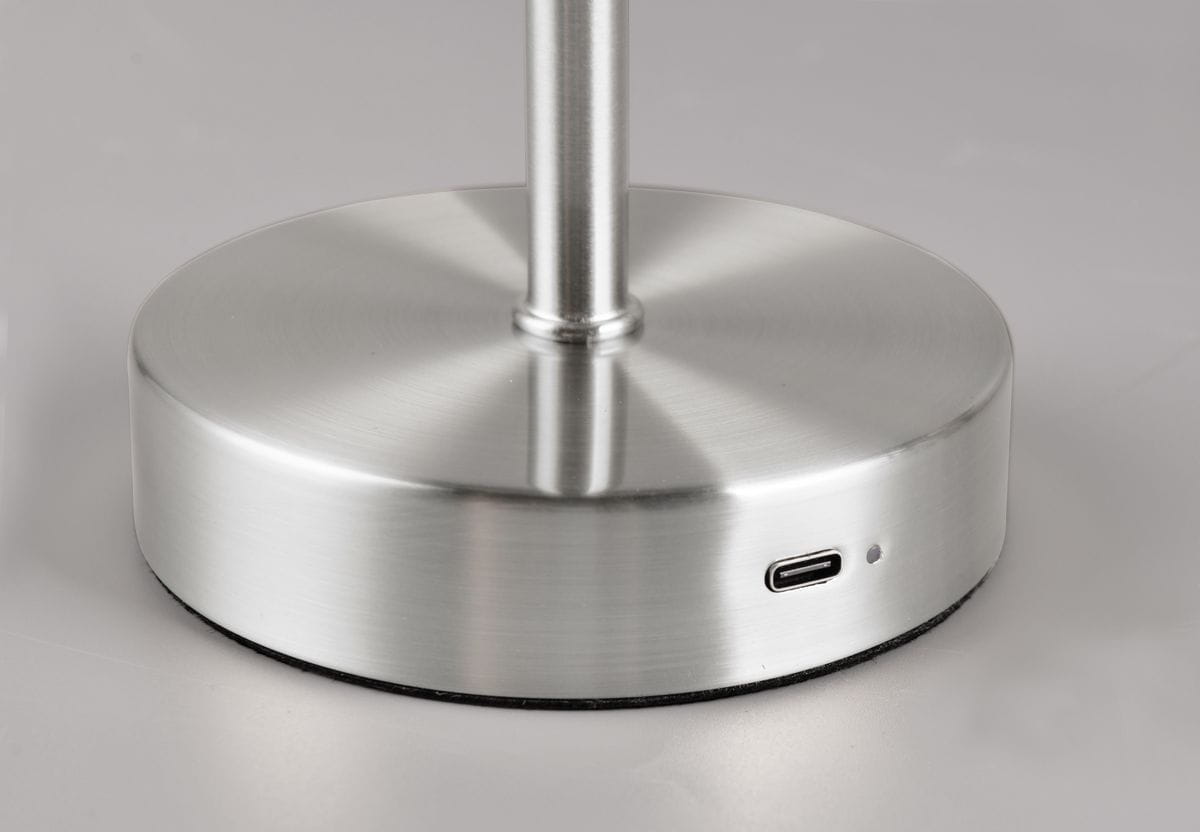 Lampa stołowa Jeff w kolorze niklowym z podstawą o okrągłym kształcie. Widoczny port USB-C do ładowania. Powierzchnia matowa, elegancka, z delikatnym połyskiem. Ujęcie z boku, ukazujące detale podstawy i teksturę materiału.