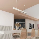 Lampa wisząca Sigi II w kolorze białym, z jedną żarówką LED o mocy 44W, zawieszona na cienkich linkach. Prosty, prostokątny kształt, umieszczona nad stołem w nowoczesnej aranżacji wnętrza. W tle widoczna jasna ściana i elementy dekoracyjne.