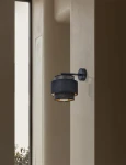 Kinkiet Amos 1xE27 w kolorze czarnym, z metalową oprawą w formie dwóch cylindrów, zamontowany na ścianie. Wnętrze klosza w kolorze złotym, widoczna żarówka. Ujęcie z boku, na tle gładkiej, jasnej ściany.