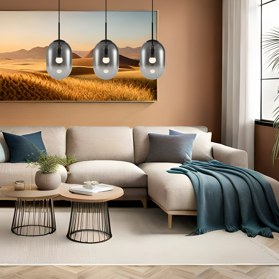Lampa wisząca Alias 3xE14 w kolorze czarnym, z trzema szklanymi kloszami o owalnym kształcie, zawieszona w nowoczesnym wnętrzu. Lampa wisi nad sofą, tworząc elegancką aranżację. Tło w ciepłych odcieniach.