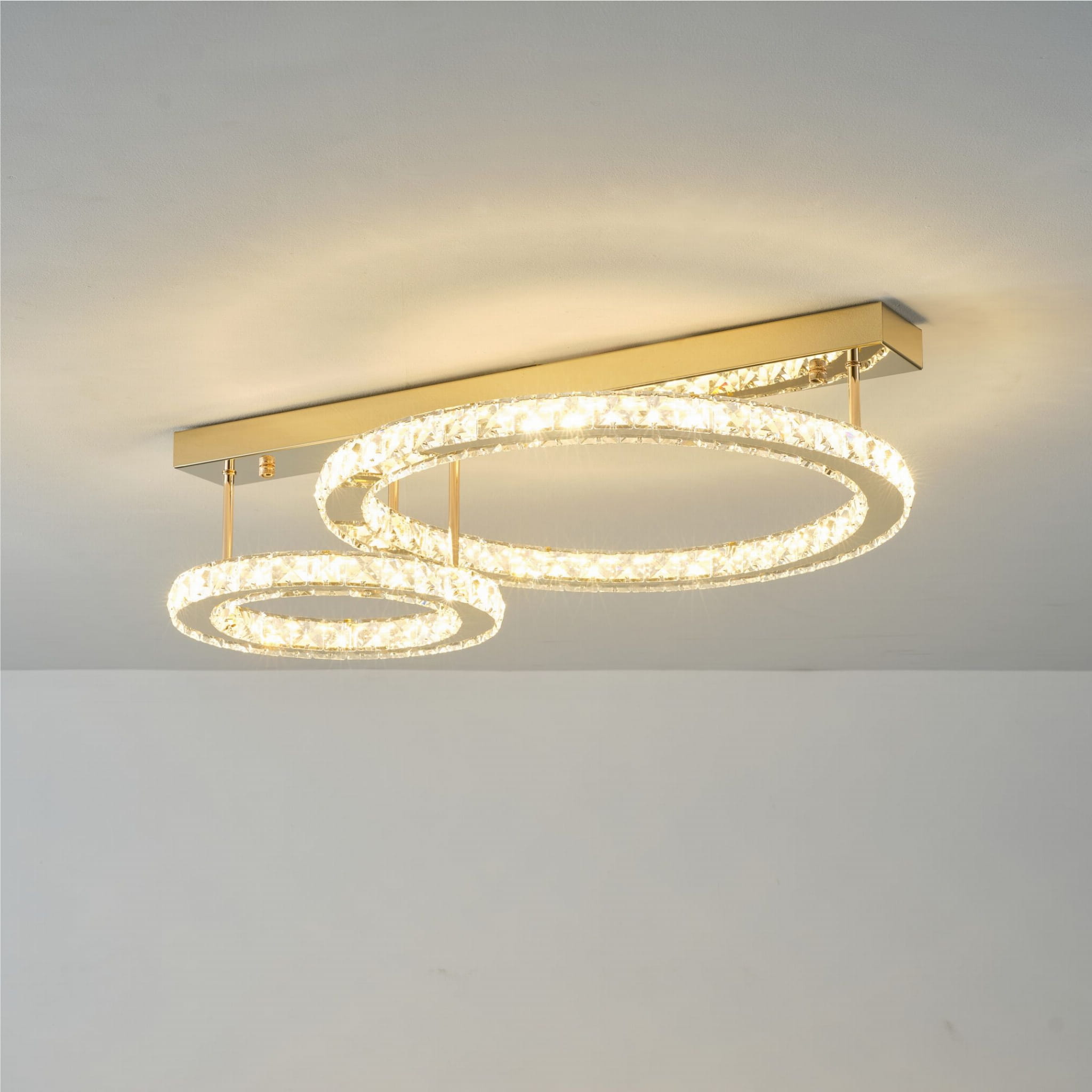 Lampa sufitowa Girona z dwoma okrągłymi kloszami LED, złota konstrukcja, z przezroczystymi elementami, zawieszona na prostokątnej podstawie. Klosze mają różne rozmiary, emitują ciepłe światło, umieszczone w nowoczesnym wnętrzu.