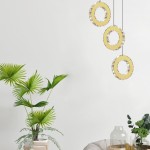 Lampa wisząca Girona 1xLED/10W w kolorze złotym, składająca się z trzech okrągłych elementów z przezroczystymi zdobieniami. Zawieszona na czarnych linkach w jasnym wnętrzu, obok rośliny doniczkowej.