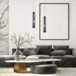 Lampa wisząca Pax 1xG9 w kolorze czarnym z przezroczystym kloszem, zawieszona na cienkim kablu. W tle widoczny nowoczesny salon z szaro-zieloną kanapą, marmurowym stolikiem i dekoracyjną gałązką w wazonie.