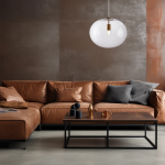 Lampa wisząca Campania 1xE27 w złotym wykończeniu z transparentnym kloszem, zawieszona nad brązową skórzaną sofą w nowoczesnym wnętrzu. W tle widoczna ściana w odcieniach brązu, tworząca elegancką aranżację.