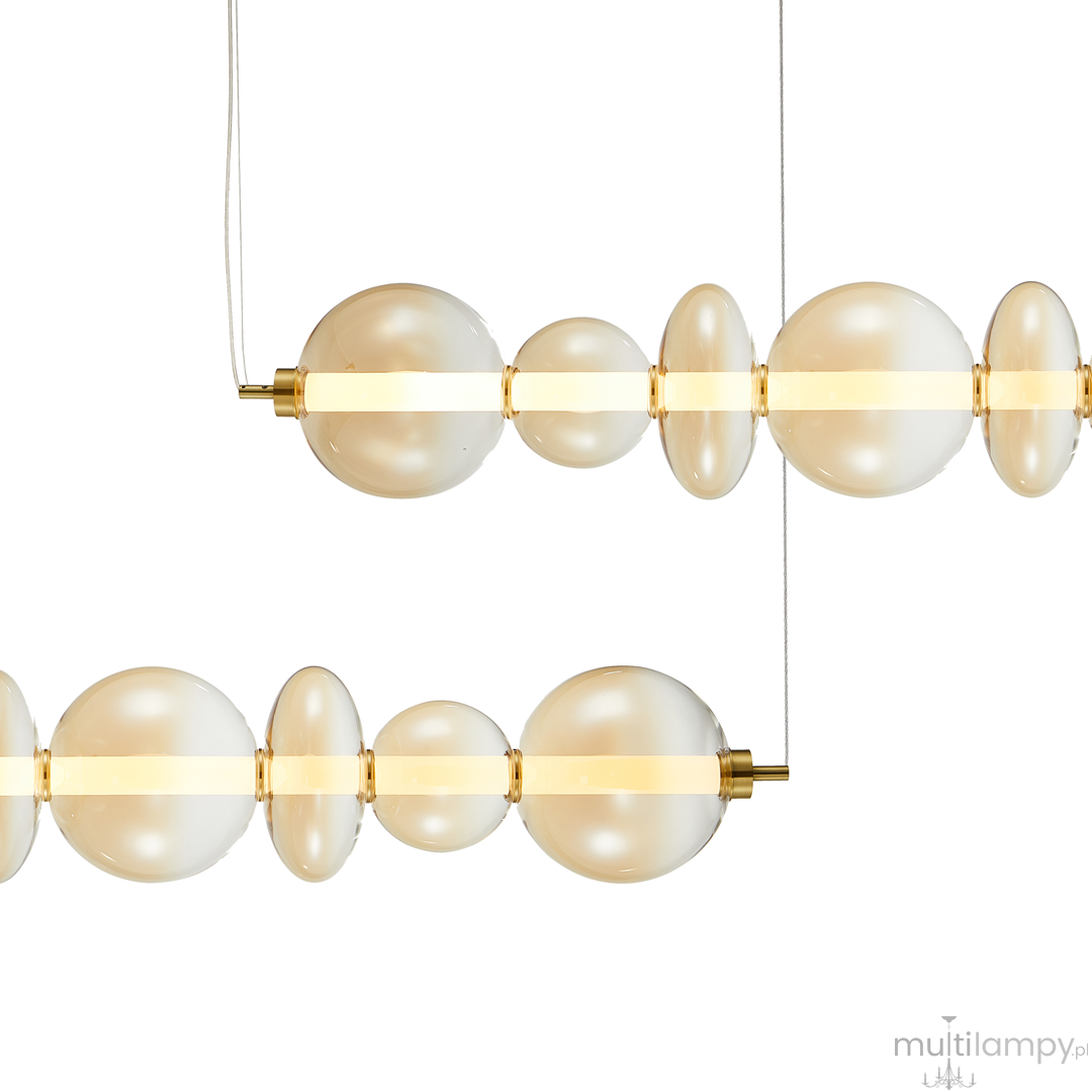 Lampa wisząca Daphne z jedną żarówką LED o mocy 40W. Złote elementy metalowe, szklane kule w odcieniu mlecznym, o różnych rozmiarach, zawieszone na cienkich linkach. Prosta, nowoczesna forma, idealna do eleganckich wnętrz.