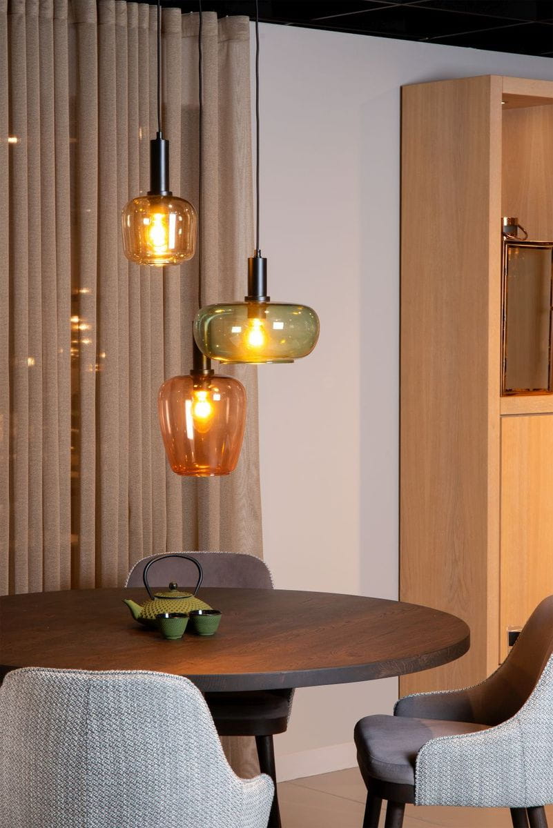 Lampa wisząca Ilona 3xE27 w kolorze czarnym z trzema szklanymi kloszami w odcieniach brązu i zieleni. Zawieszona na cienkim przewodzie w nowoczesnym wnętrzu, nad okrągłym stołem. Widoczne ciepłe światło żarówek.