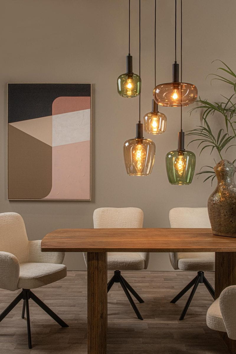 Lampa wisząca Ilona z pięcioma kloszami w różnych kolorach (przezroczysty, zielony, brązowy) zawieszona na czarnych przewodach. Widoczna w aranżacji nad drewnianym stołem w jadalni, z tłem w stonowanych kolorach i dekoracyjnym obrazem.