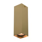 Lampa sufitowa Ander w kolorze mosiądzu, o prostokątnym kształcie, zamontowana w pionie. W górnej części znajduje się miejsce na żarówkę GU10. Dół lampy otwarty, co umożliwia skierowanie światła w dół. Tło białe, minimalistyczne.