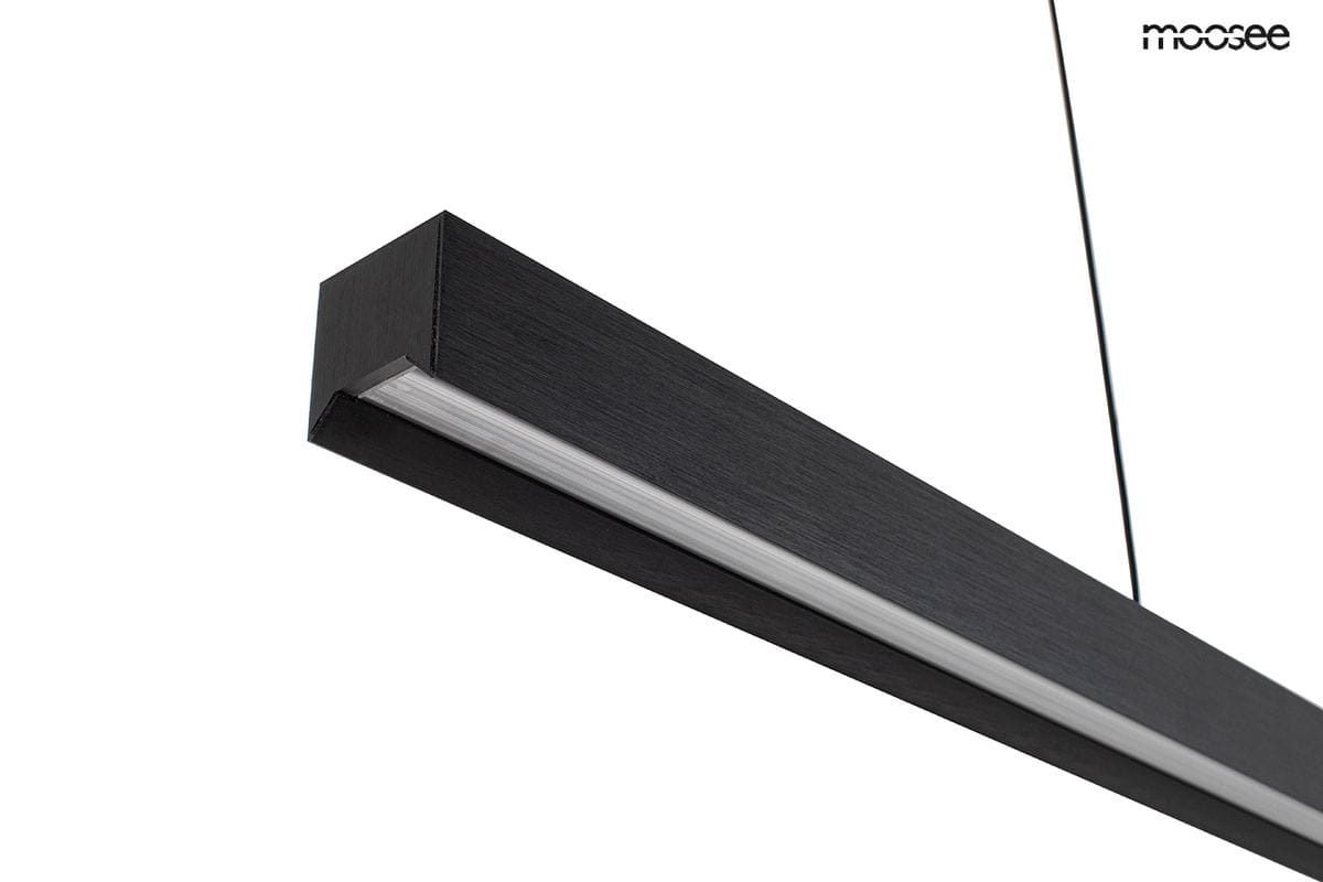 Lampa wisząca Liner, czarna, o prostokątnym kształcie, wykonana z matowego materiału, z wbudowanym źródłem światła LED 32W. Ujęcie z boku, z widocznym detalem przezroczystego klosza. Kabel zawieszenia w czarnym kolorze.