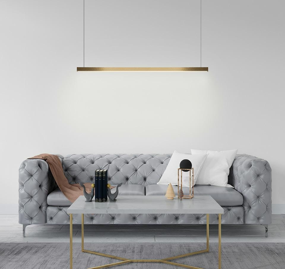 Lampa wisząca Linus 80 w kolorze złotym, z jedną żarówką LED 15W, zawieszona nad szarym, pikowanym sofą. W tle jasna ściana, a na stole znajduje się kilka książek i dekoracji.