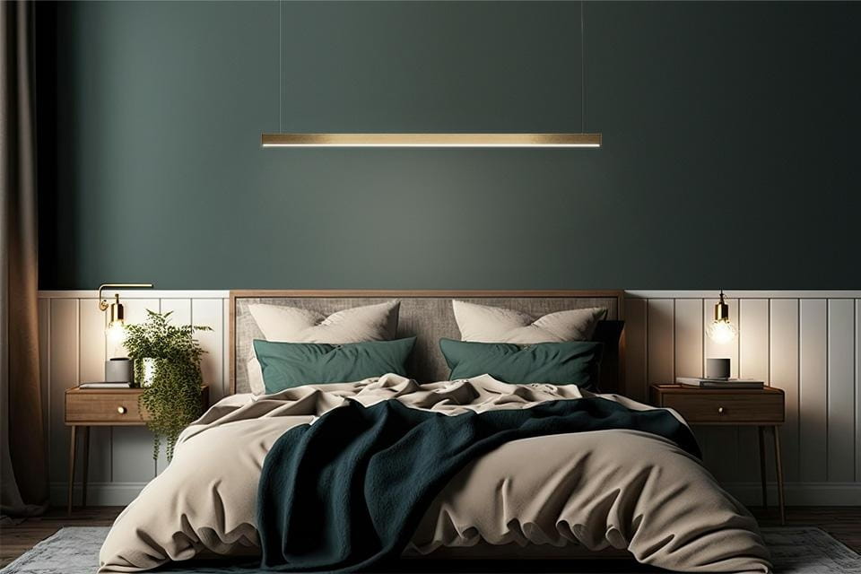 Lampa wisząca Linus 100 w kolorze złotym, z 1 źródłem światła LED o mocy 17W. Zawieszona nad łóżkiem w nowoczesnej sypialni, otoczona poduszkami w odcieniach zieleni i beżu, z drewnianymi meblami w tle.