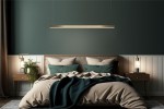 Lampa wisząca Linus 100 w kolorze złotym, z 1 źródłem światła LED o mocy 17W. Zawieszona nad łóżkiem w nowoczesnej sypialni, otoczona poduszkami w odcieniach zieleni i beżu, z drewnianymi meblami w tle.