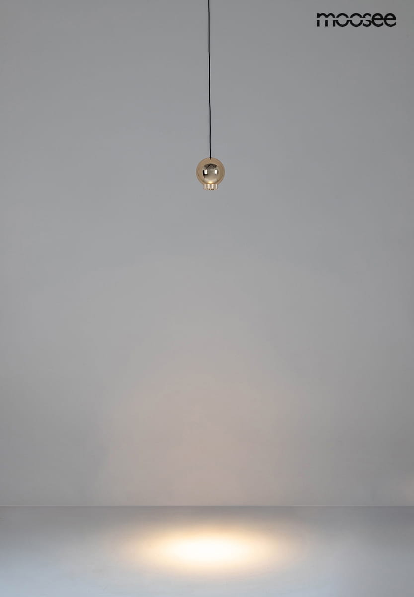 Lampa wisząca Ojo w kolorze złotym, z pojedynczym źródłem światła LED 7W. Prezentowana w zbliżeniu, zwisająca z czarnego kabla na jednolitym tle. Kształt okrągły, z połyskującą powierzchnią, emitująca ciepłe światło na powierzchnię poniżej.