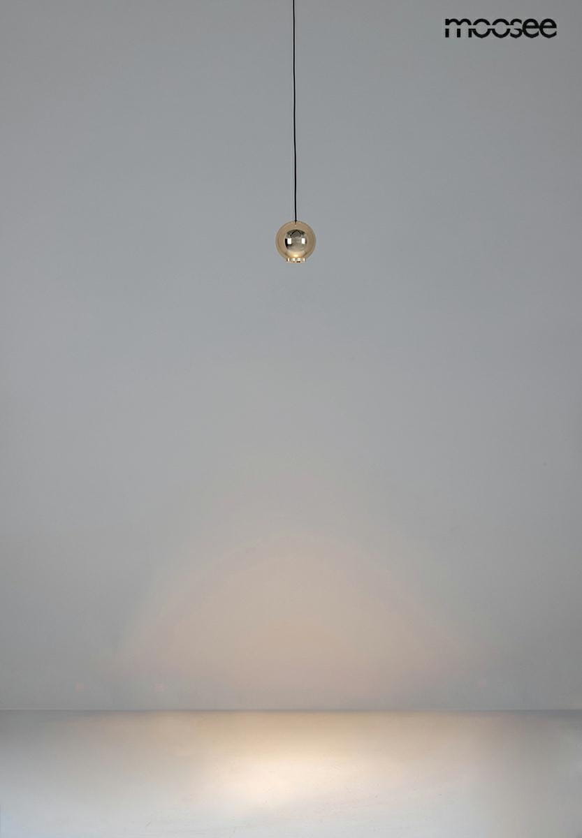 Lampa wisząca Ojo w kolorze złotym, z jedną żarówką LED o mocy 7W. Ujęcie z góry, lampa zawieszona na cienkim przewodzie w minimalistycznym otoczeniu. Widoczne subtelne odbicia światła na powierzchni pod lampą.