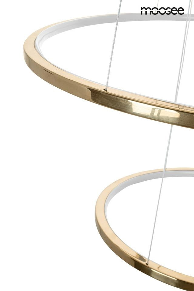 Lampa wisząca Ring Slim L w złotym kolorze, z okrągłym kształtem. Widoczne dwa pierścienie, jeden wewnętrzny z białym wykończeniem, zawieszone na cienkich żyłkach. Produkt z pięcioma diodami LED, z pilotem do zdalnego sterowania.