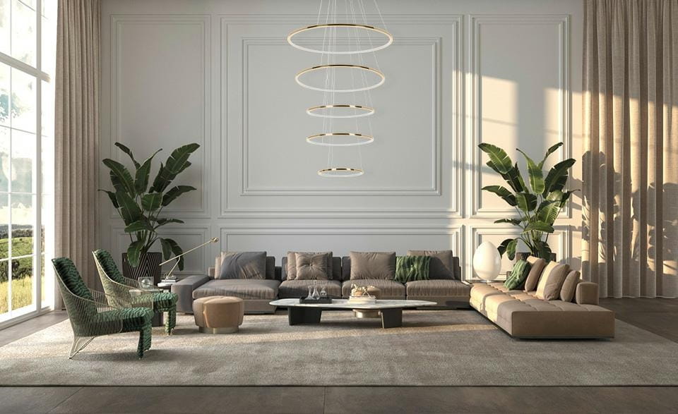 Lampa wisząca Ring Slim L w kolorze złotym, z pięcioma okrągłymi źródłami LED, zawieszona na cienkich linkach, umieszczona w nowoczesnym wnętrzu z dużymi oknami, stylowymi meblami i roślinami w tle.
