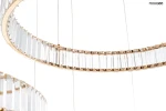 Lampa wisząca Liberty 3B z trzema źródłami LED, złota, z przezroczystymi, prostokątnymi kryształami ułożonymi w okrąg. Produkt zawieszony na cienkich linkach, ukazujący elegancki design oraz nowoczesne wykończenie.
