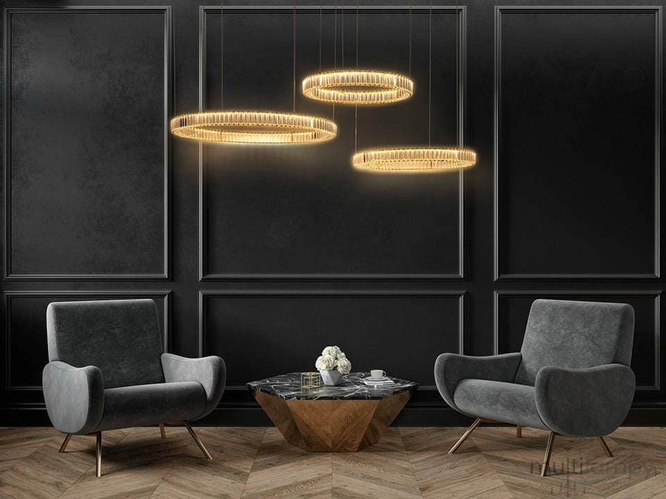 Lampa wisząca Liberty 3B z trzema okrągłymi kloszami LED w złotym kolorze, zawieszona w równych odstępach. W tle ciemna ściana oraz nowoczesne, szare fotele obok stołu z drewnianą podstawą i marmurowym blatem.