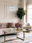 Lampa wisząca Allisia 80, 1xLED/43W, w złotej oprawie, z dekoracyjnym kloszem z przezroczystego szkła, zawieszona nad stołem w eleganckim wnętrzu z kanapą i rośliną w tle.