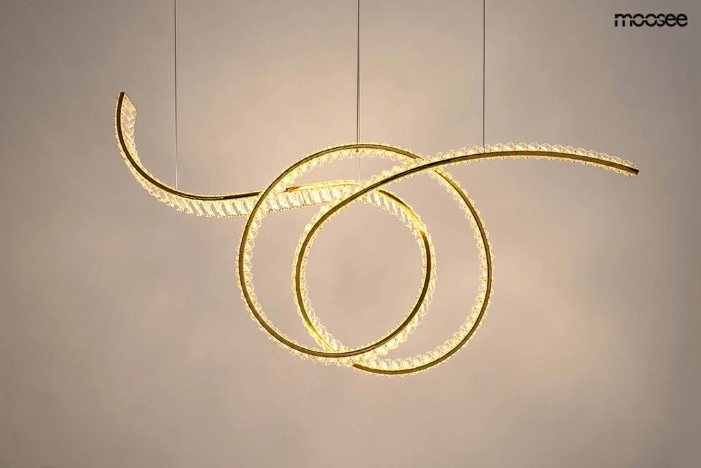 Lampa wisząca Wave 120 w kolorze złotym z jednym źródłem LED o mocy 28W. Posiada unikalny, spiralny kształt z przezroczystą fakturą, zawieszona na cienkich linkach, tworzy nowoczesną i elegancką aranżację. Tło w jasnym odcieniu.