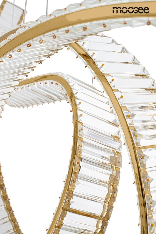 Lampa wisząca Wave 120 o złotej oprawie, z diodą LED 28W. Posiada dwa spiralne pierścienie wykonane z przezroczystego materiału, ozdobione drobnymi, miedzianymi detalami. Ujęcie z boku, na białym tle.