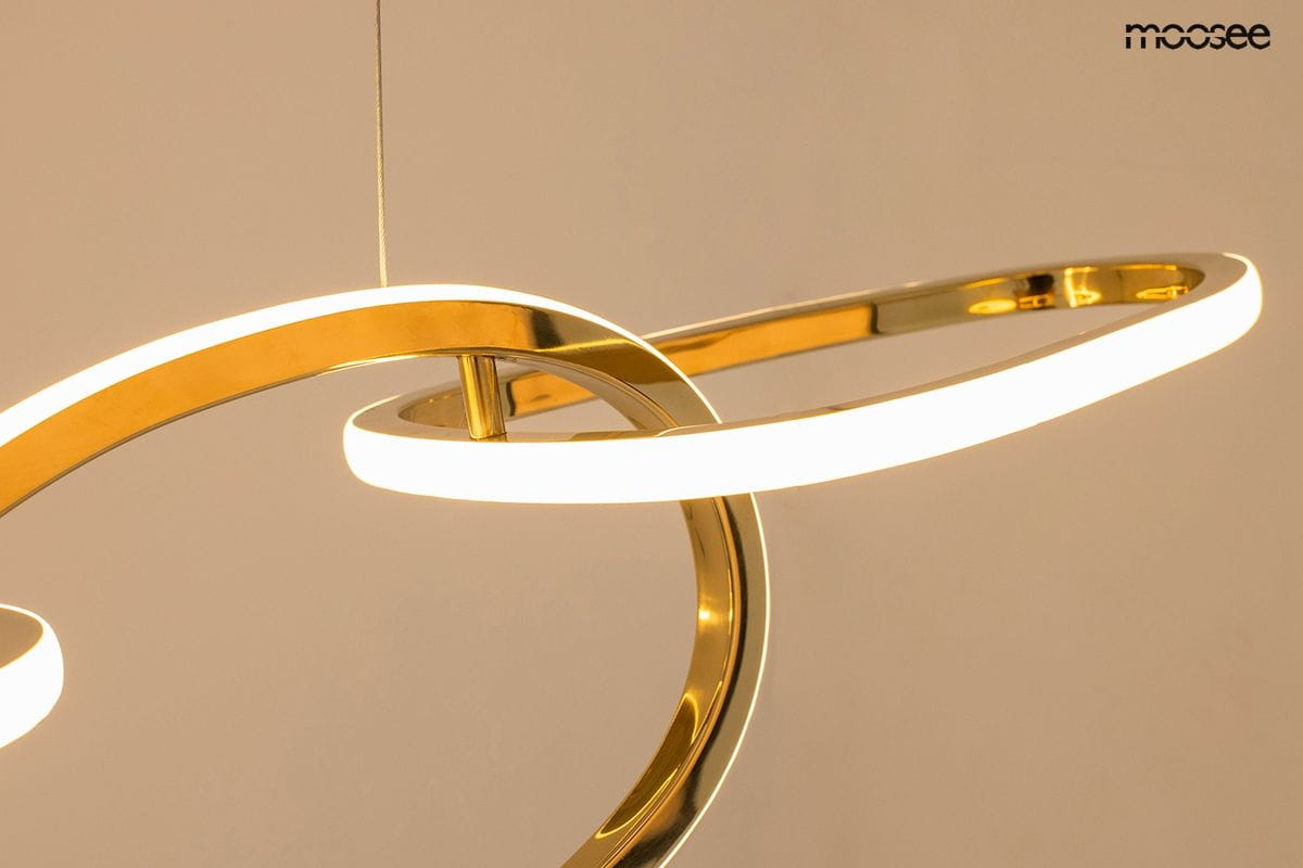Złota lampa wisząca Jazz z pięcioma źródłami LED, o nowoczesnej formie z okrągłymi, lśniącymi elementami. Ujęcie z góry, pokazujące detale konstrukcji i podświetlenie. Tło w jasnym kolorze, skupiające uwagę na lampie.