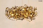 Lampa wisząca Monete 60, złota, o okrągłym kształcie, z 12 źródłami światła G4. Wykonana z metalowych, dekoracyjnych elementów w formie okrągłych, błyszczących detali, zawieszona na cienkich linkach w jasnym otoczeniu.