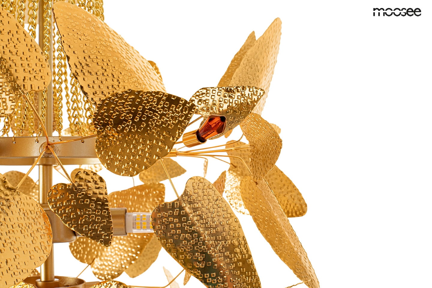 Lampa wisząca Paradiso w złotym kolorze, z detalami w kształcie liści o fakturze. Posiada cztery uchwyty na żarówki G9. Ujęcie z boku, pokazujące dekoracyjne elementy oraz mocowanie. Tło białe, co podkreśla elegancję lampy.