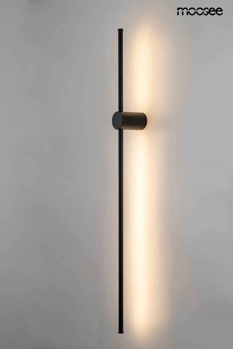 Kinkiet Ombre 100 w kolorze czarnym, z jedną diodą LED o mocy 12W. Produkt ma prostą, pionową konstrukcję z metalowym mocowaniem i emitującym ciepłe światło panelem. Ujęcie frontalne na tle jasnej ściany.